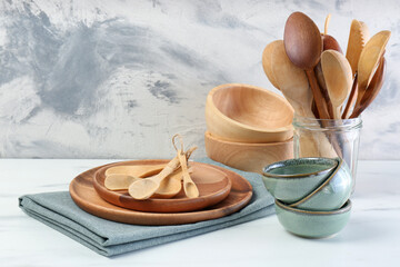 Different dishware and utensils on white marble table against textured wall