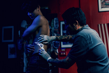 Close-up hands of master Tattoo artist in white gloves sticking paper with pattern on client hand on a Man waist, in a modern in Studio lowlight.