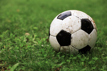 Dirty soccer ball on green grass outdoors, space for text