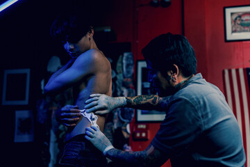 Close-up hands of master Tattoo artist in white gloves sticking paper with pattern on client hand on a Man waist, in a modern in Studio lowlight.