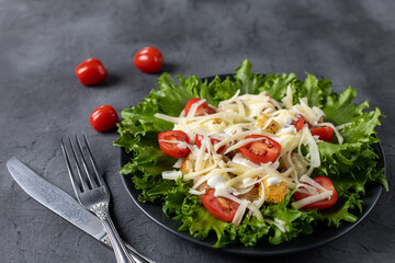 Traditional caesar salad with chicken on a black plate on black table with napkin fork and knife.