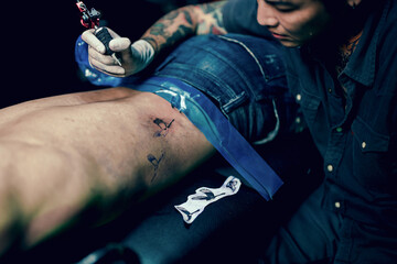 Professional tattooist makes the tattoo on a men waist, focusing on tattoo machines in a modern studio lowlight.