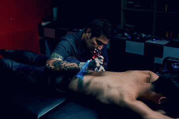 Professional tattooist makes the tattoo on a men waist, focusing on tattoo machines in a modern...