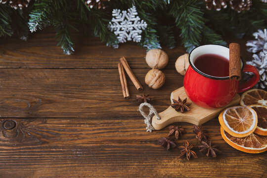Christmas mood, holiday atmosphere. Red cup of coffee, fir branches with cones, walnuts, cinnamon, star anise on a wooden table background.