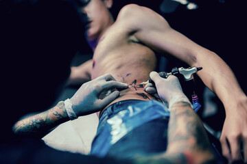 Professional tattooist makes the tattoo on a men waist, in a modern studio lowlight.