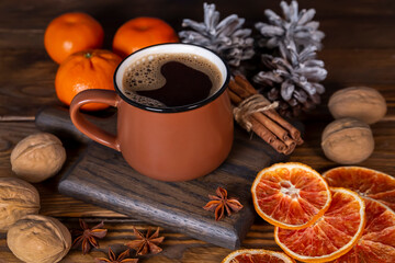 Christmas mood, holiday atmosphere. A cup of coffee, pine cones, walnuts, cinnamon, star anise and tangerines on a wooden table background.