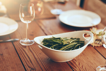 Thanksgiving, green beans and food with a place setting on a dining room table for a celebration event. Party, dish and dinner with a bowl on a wooden surface in celebration or holiday tradition