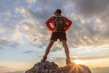 Young male hiker with backpack enjoying sunrise on top mountain park.