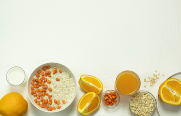 oatmeal porridge in a white plate with yellow berries, juice and orange on a white background