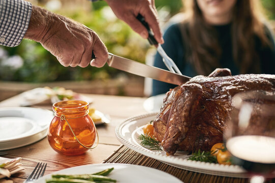 Food, hands and turkey with family at a table in celebration of thanksgiving, tradition and lunch meal on a patio. Chicken, hand and man carving meat to share with friends at christmas party outdoor