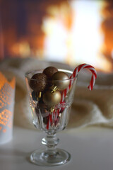 Glass with Christmas ornaments, cup of tea, cookies, candles and knitted blanket by the fireplace. Cozy Christmas at home.