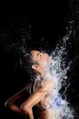 Tanned skin Asian woman in bikini poses in aqua studio. Splash Drops of water spread to body. Fun emotion female girl on water attack fluttering and stop motion freeze shot, black background isolated
