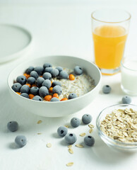 oatmeal porridge in a white plate with blueberries, a glass of orange juice and milk on a white background.