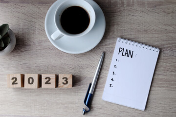 Happy New Year concept. Wooden cube with the number 2023 with notebook plan and coffee on office desk.