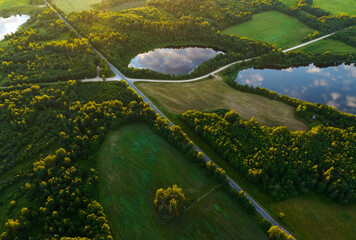 Highway through forest with pine trees and lakes, aerial view. Road with forrest trees and car. Forest road for transpotrs. Aerial above view of freeway. Asphalt road near lake in village, top view.