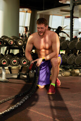 Fototapeta na wymiar Athletic young man with battle rope doing exercise in functional training fitness gym