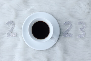 The numbers 2023 with mug of coffee on furry white background. Flat lay, new year winter holiday concept. 
