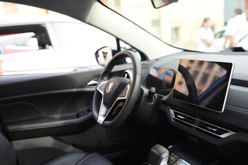 Fototapeta na wymiar Steering wheel of an electric modern car. Car interior. Driver's seat with steering wheel and electronic display, navigation, climate control and other options. Perforated leather and seat ventilation