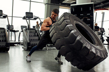 Muscular fitness man moving large tire in gym center, concept lifting, workout training.