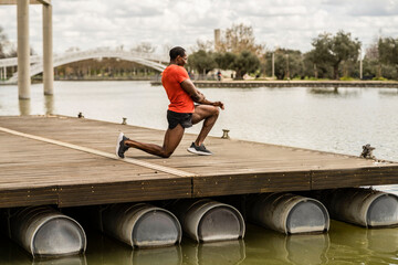Senior african american man stretching legs in a park with a lake outside