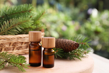 Fototapeta na wymiar Bottles of pine essential oil, cone and branches on wooden table, closeup. Space for text