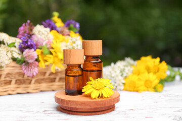 Bottles of essential oils and beautiful flowers on white wooden table
