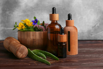 Glass bottles of aromatic essential oil and mortar with different herbs on wooden table