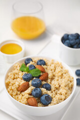 Bowl of delicious cooked quinoa with almonds and blueberries on white table, closeup