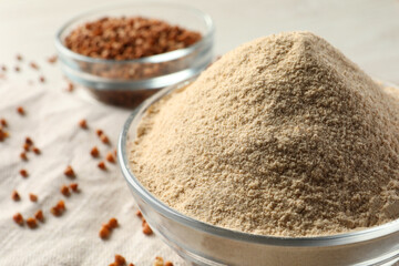 Glass bowl of buckwheat flour and cloth on white table, closeup