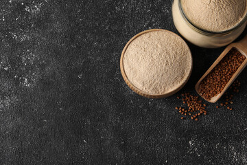 Flat lay composition with buckwheat flour and grains on black table. Space for text