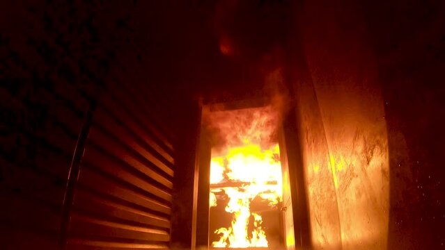 Flames erupt inside a fire training simulator and flashover along the ceiling. POV from firefighter looking up at flame and back down to level. Tilt up, tilt down.