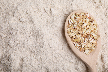 Spoon with oat flakes on flour, top view. Space for text