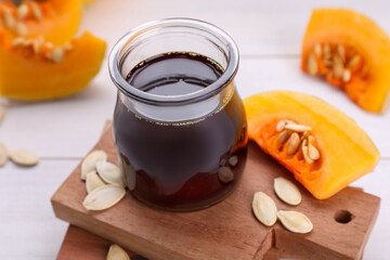 Fresh pumpkin seed oil in glass jar on white wooden table