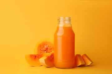 Tasty pumpkin juice in glass bottle and cut pumpkin on orange background