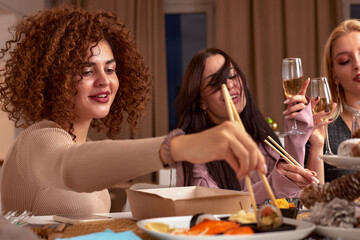 Discussing the latest gossips. Three beautiful young women talking and smiling while drinking wine and sitting on the couch together