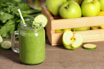 Mason jar of fresh green smoothie and ingredients on wooden table, space for text