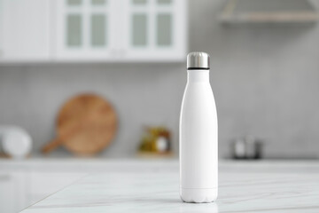 Stylish thermo bottle on white table in kitchen. Space for text