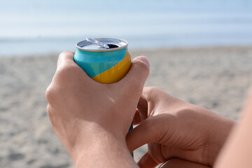 Woman holding aluminum can with beverage on beach, closeup