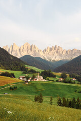 Fototapeta na wymiar Stunning view of the Funes Valley (Val di Funes) with the Santa Maddalena Church and the mountain range of the Puez Odle Nature Park in the distance during a beautiful sunset...