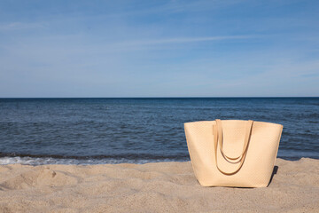 Fototapeta na wymiar Stylish summer bag on sand near sea, space for text. Beach accessory