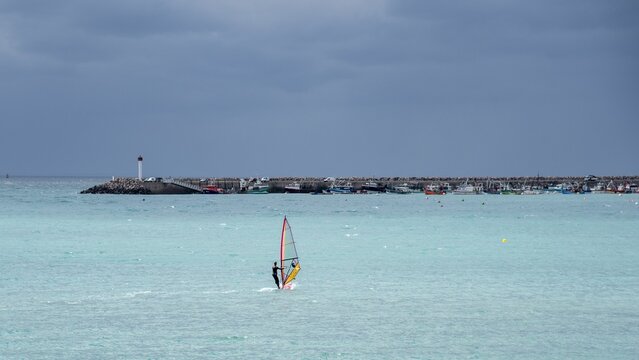 Person windsurfing in the ocean with a lighthouse and a cloudy sky in the background