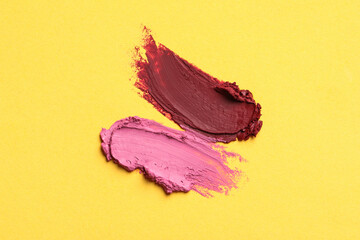 Smears of bright lipsticks on yellow background, top view