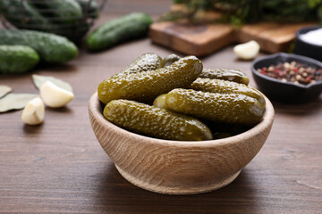 Bowl of pickled cucumbers and ingredients for food preservation on wooden table, closeup