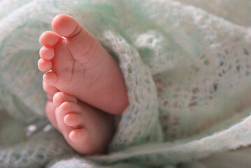 Cute newborn baby covered in turquoise crocheted plaid on bed, closeup of legs