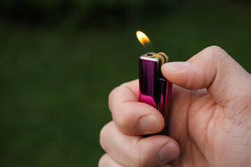 Man holding lighter with burning flame outdoors, closeup. Space for text - obrazy, fototapety, plakaty