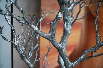 Dekoration mit silbernen Baumästen- und zweigen vor grauem und beige-rotem Hintergrund 