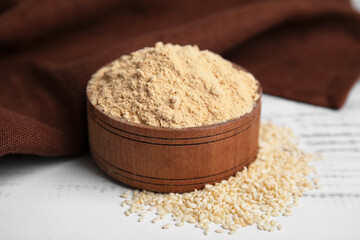 Sesame flour in bowl on white wooden table, closeup