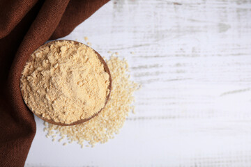Sesame flour in bowl on white wooden table, top view. Space for text