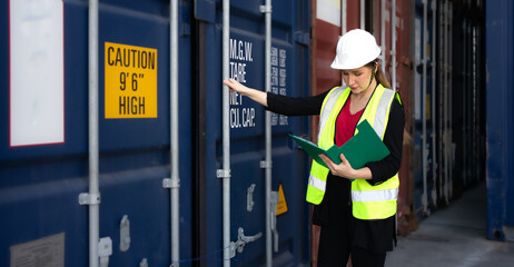 Female foreman supervisor wears safety hardhat inspecting container cargo at warehouse storage...
