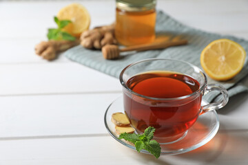 Cup of delicious ginger tea and ingredients on white wooden table, space for text